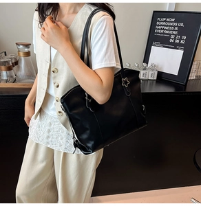 Detail of black faux leather tote bag with silver star buckle and long shoulder straps