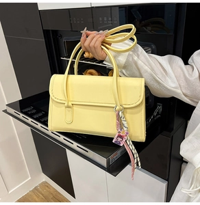 Detail of a yellow PU leather baguette bag with a decorative woven cartoon charm