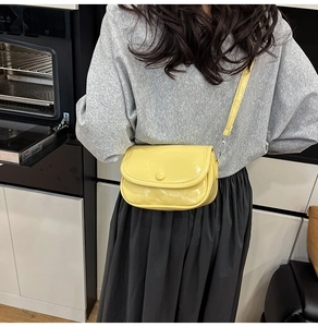 Detail showing bright yellow patent leather saddle bag with silver metal hooks and buckle