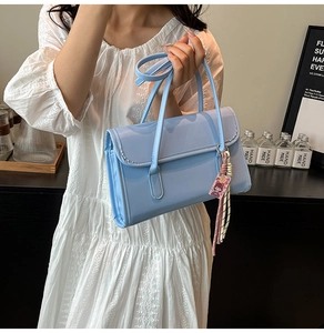 Close-up of light blue rectangular handbag with pink tassel charm and smooth finish