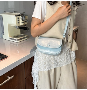 Detailed view of light blue glossy crossbody bag with round buckle on model
