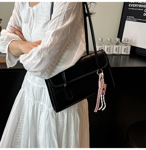 Close-up of a vintage black rectangular baguette bag with decorative woven pendant