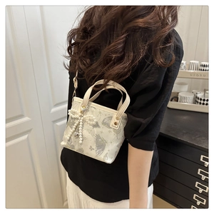 Detailed view of cream butterfly print bucket bag with pearl bow charm worn by model