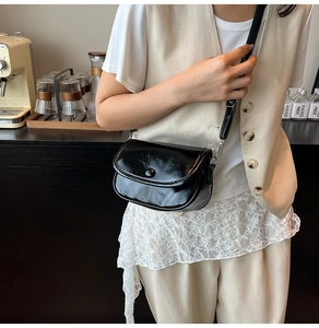 Close-up of a mini black glossy leather crossbody bag worn in a cozy cafe setting