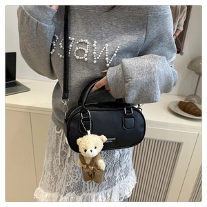 Detail of black litchi texture small square bag with a cute teddy bear plush pendant charm