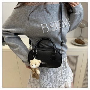 Close-up of black lychee leather bowling bag featuring a cute teddy bear charm