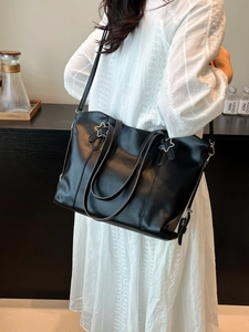 Large black faux leather tote bag with silver star accents shown on a model's shoulder