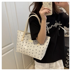Detailed view of white tote bag with black bow patterns and gold brand logo plaque