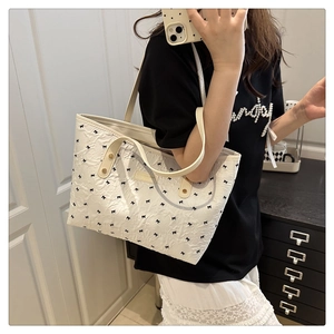 Detail of white bubble texture tote bag with black bow patterns and leather straps