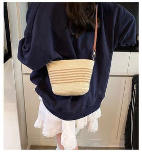 Close-up of a woven straw bucket bag with brown stripes worn by a model in casual style