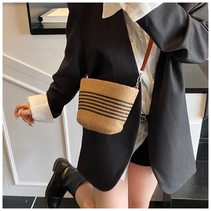 Detail of straw bucket bag with black stripes and leather strap on a fashion model
