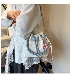 Detail of a wavy texture bucket bag with blue braided handle and charm on a model