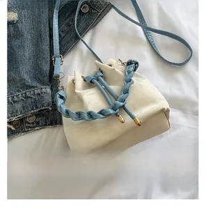 Detail of drawstring bucket bag featuring blue woven handles and cream glossy finish