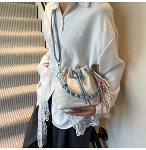 Detail of cream leather bucket bag with blue straps and braided handle on shoulder