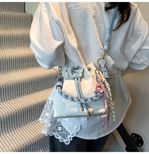Detail of white and blue drawstring bucket bag featuring a woven handle and side charms
