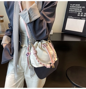Detail of white drawstring bucket bag with pink woven handle and metal hardware hooks