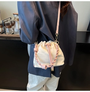 Detail of cream drawstring bucket bag with pink woven handle and long shoulder strap