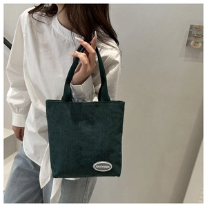 Detail shot of the dark green corduroy texture and brand label on a casual tote bag