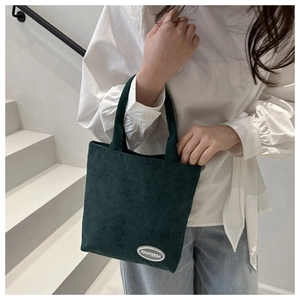 Detail of dark green corduroy tote bag with white logo patch on minimalist background