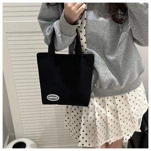 Close-up of a black corduroy tote bag with a white logo label on a daily outfit