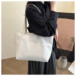 Detailed view of large white woven faux leather tote bag worn by a model in a minimalist room