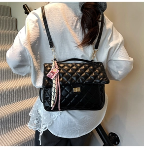 Detail of black quilted tote bag with golden twist lock and pink cartoon charm