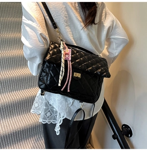 Detail of black quilted leather backpack featuring gold twist lock and a pink charm