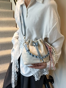 Chic beige bucket bag with blue woven handle and shoulder strap worn by a model