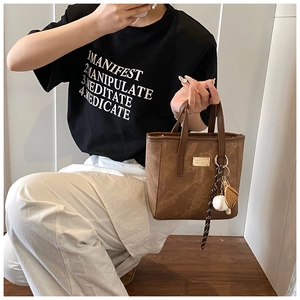 Details einer braunen Wildleder-Beuteltasche mit Baseball-Anhänger und goldenem Logo-Schild