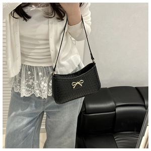 Detailed view of black woven shoulder bag featuring a decorative gold bow buckle detail