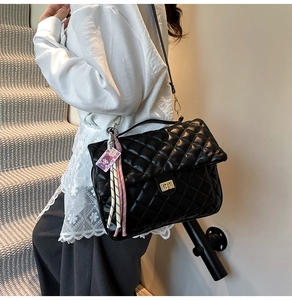 Close-up of black quilted tote bag with golden lock and purple girl pendant accessory