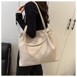 Detail of a large beige canvas tote bag showing the fashion leather label and stitching