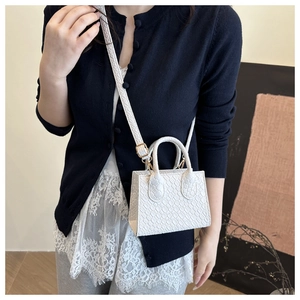 Close-up of white embossed leather mini bag with gold hardware and adjustable strap