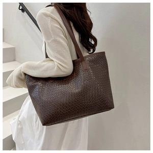 Detail view of deep brown large tote bag with woven texture on a shoulder model