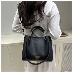 Minimalist black tote bag featuring a golden metallic handle and triangular logo detail