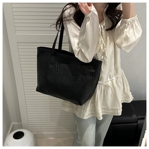 Close-up of black woven tote bag with silver logo on shoulder of fashion model