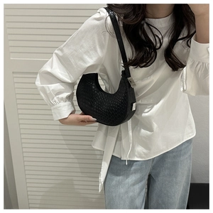 Detail of black crescent shoulder bag with embossed texture and silver buckle on model
