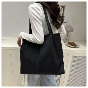 Close-up of minimalist black canvas tote bag with wide shoulder strap and structural seams