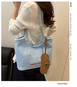 Detail of light blue denim tote bag with puppy embroidery and brown glasses case charm