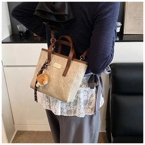 Detail der beigen Canvas-Tasche mit braunem Rand, Goldlogo und Kugelfisch-Anhänger