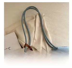 Detail of light blue denim tote with comfortable rolled handles and brown leather accents