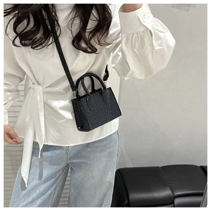 Detail view of black ostrich embossed mini crossbody bag shown on a model
