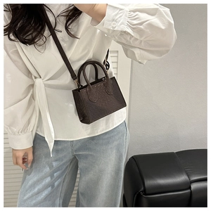 Detail of dark brown faux crocodile skin crossbody mini bag worn by a fashion model