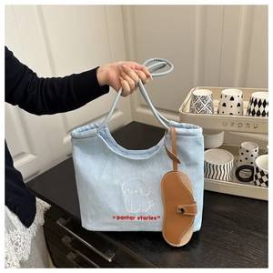 Detail of light blue denim tote with dog embroidery, drawstring closure, and brown pouch