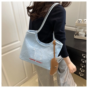 Detail of light blue denim tote bag with cartoon dog embroidery and brown leather charm