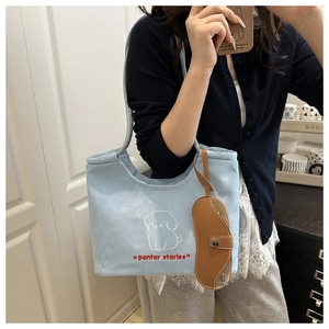 Close-up of light blue denim tote bag with puppy embroidery and leather glasses charm