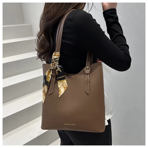 Detail of dark brown tote bag with silk scarf handle and golden brand lettering