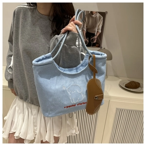 Detail of light blue denim tote bag with puppy embroidery and brown leather charm