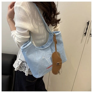 Blue denim tote bag detail featuring cartoon embroidery and leather glasses case charm