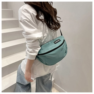 Sac bandoulière demi-lune en nylon sarcelle porté par un mannequin en tenue décontractée